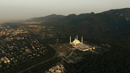 MargallaDrone Orbits around Faisal Mosque durinfg sunrise, the Mosque is one of the biggest in the world and its right between green hills and Islamabad city, good establishing shot.