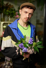 Love, dating or romance concept. Hooligan male in peaked cap and tracksuit with toothpick in mouth holding spring flower bouquet standing indoor in flower store. High quality photo