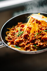 Cooked Italian spaghetti being put into hot bolognese sauce in the pan on kitchen