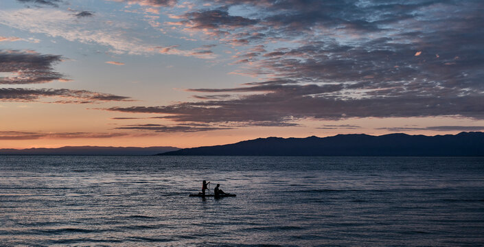 Silhouette of couple on SUP board against colorful sunset. Barguzinsky Bay of Lake Baikal, Russia.