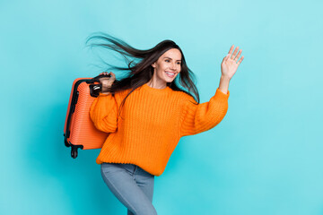 Photo of pretty cheerful girl hold suitcase look arm palm waving hi empty space isolated on cyan color background - obrazy, fototapety, plakaty