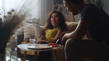 Woman with a physical disability and man joking and laughing together while sitting on a couch and having a dinner at home