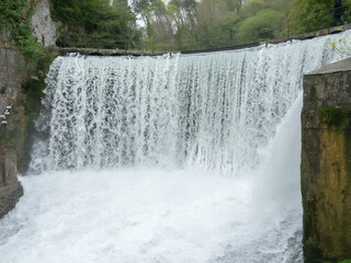 Powerful splashing stream of a waterfall. The waterfall flows down from the dam in the park