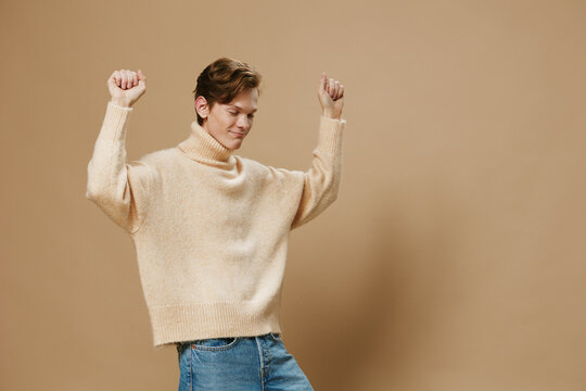 a happy, joyful young man with red hair, in a long sweater, dances merrily. Studio photography on a plain background with empty space for an advertising layout