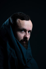 dramatic religious portrait of a bearded guy in a black cape on a dark background