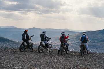 Group of motorcyclists travel offroad, standing on mountain top discuss and enjoying view