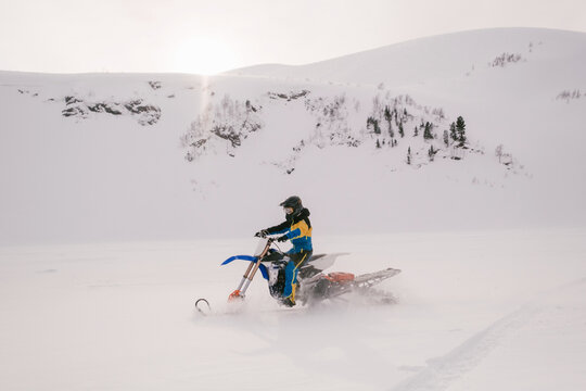 Female Rider on winter motorcycle snowbike in beautiful mountain landscape during sunset