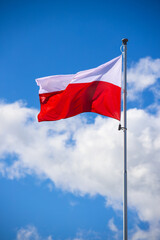 Polska flaga biało-czerwona powiewająca na maszcie na tle błękitnego nieba