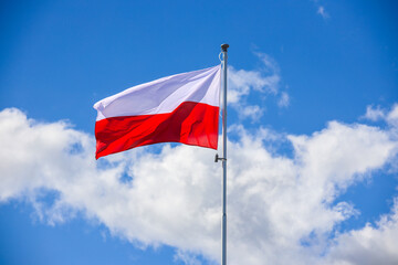 Polska flaga biało-czerwona powiewająca na maszcie na tle błękitnego nieba - obrazy, fototapety, plakaty