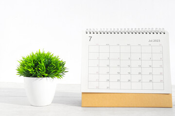 july 2023 Desktop calendar for planners and reminders on wooden table with plant pots on a white...