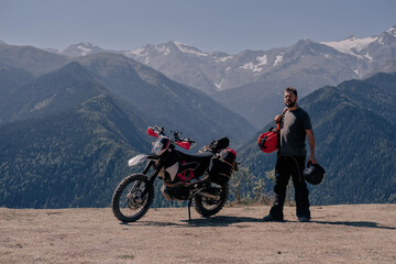 Male motorcyclist traveler standing near motorcycle with large hermetic bag on his shoulder. Moto travel in mountains