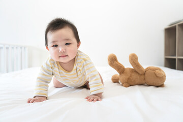 Portrait of cute little asian baby girl wearing bodysuit lying on white beedsheets at home.