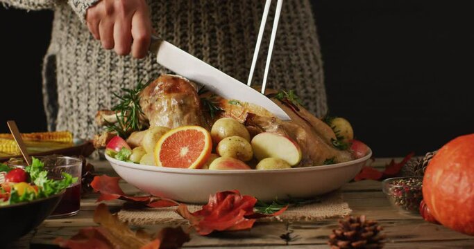 Video of midsection of caucasian woman cutting roasted turkey on table with autumn decoration
