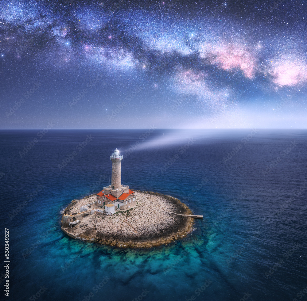 Wall mural lighthouse on smal island in the sea and milky way at night in summer. aerial view of beautiful ligh