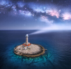 Lighthouse on smal island in the sea and Milky Way at night in summer. Aerial view of beautiful...