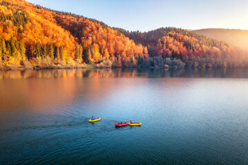 Aerial view of people on floating colorful boats on blue lake in mountains with red forest at...