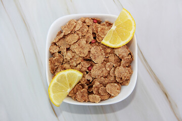dry wheat diet muesli and yellow lemon slices in a ceramic plate on a gray marble background