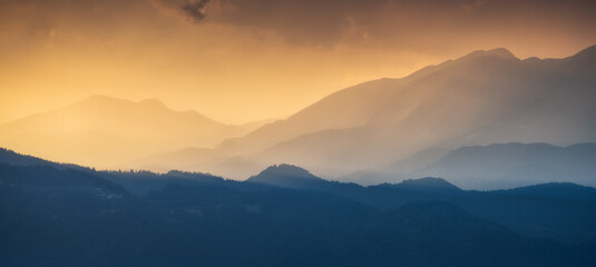 Naklejka na ściany i meble Amazing silhouettes of a mountains at colorful sunset in summer in Slovenia. Landscape with mountain ridges in fog, golden sunlight and clouds in the evening. Nature. Hills in sunlight. Scenery