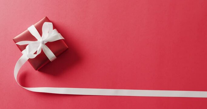 Video of red christmas gift with white ribbon and copy space on red background