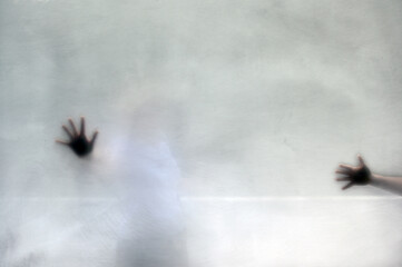 The shadows of two female hands behind frosted glass. Violence against women.