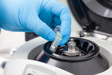 Closeup of a scientist hand placing a tube into an small table centrifuge. Spin column-based...