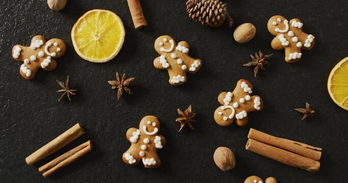 Video of smiling gingerbread men and spices, slices of orange and nuts over black background
