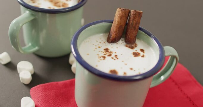 Video of cups of hot chocolate with cinnamon over grey background