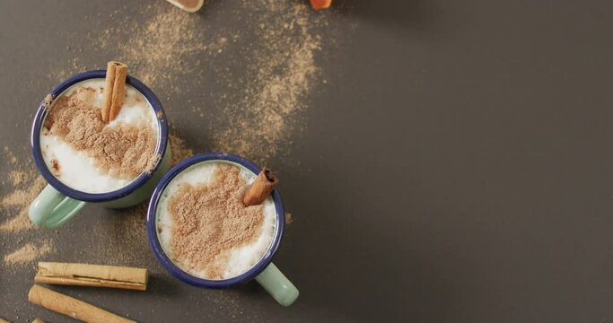 Video of cups of hot chocolate with cinnamon over grey background