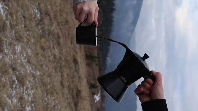 Person pouring out coffee from moka pot into cup outdoors with fog background