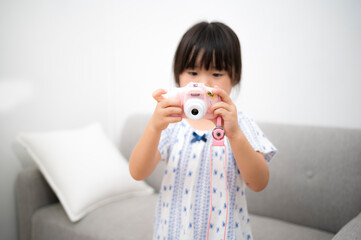 自宅の部屋でおもちゃのカメラを撮って遊ぶ女の子