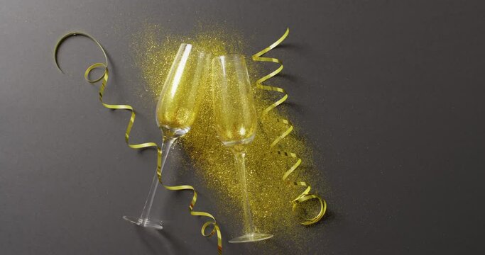 Video of two champagne flute glasses with gold streamers and glitter on black, with copy space