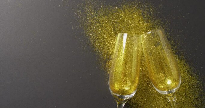 Video of two champagne flute glasses with gold glitter on black, with copy space