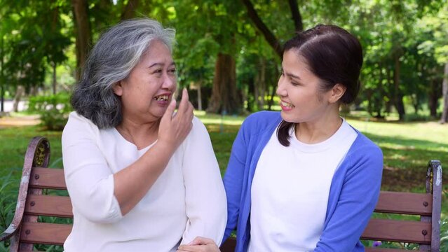Happy senior mother with gray hair talk and laugh with daughter or caregiver in the park. Concept of happy retirement with care from a caregiver and Savings and senior health insurance, senior care