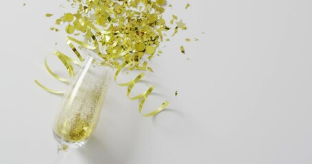 Video of champagne glass with gold streamers and confetti on white, with copy space