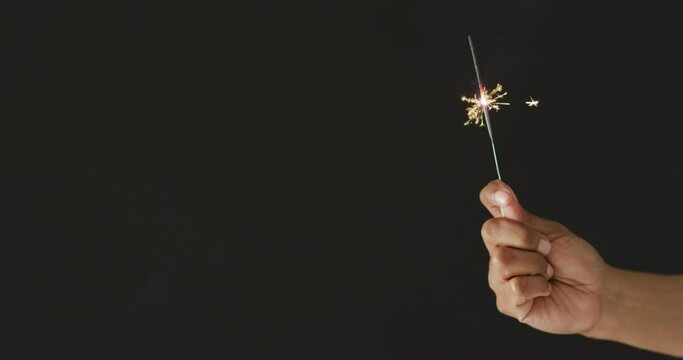Video of hand of african american person holding lit sparkler on black background, with copy space