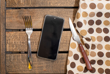 tenedor, servilleta y cuchillo, en vez de plato movil. Concepto tecnología y movil alimentación, movil en las comidas, influencia de las redes sociales en la forma de alimentarnos. - obrazy, fototapety, plakaty