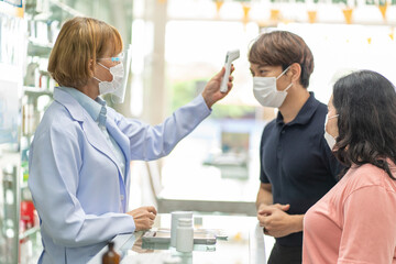Obraz premium white female pharmacist uses a digital thermometer to measure the temperature. Female Chan customers come in to buy medicines to check if they have a fever or not before giving them.