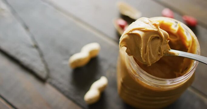 Video of close up of peanut butter and peanuts on wooden background