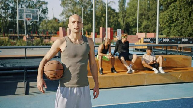 Bald man holds basketball ball standing on outdoor court