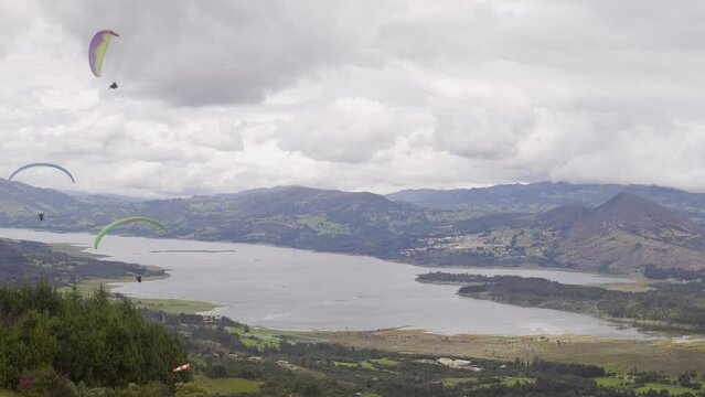 three paraglides fly near a reservoir and move away from the camera