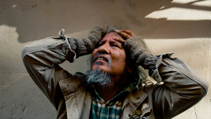 Fototapeta premium Close Up The face of a dirty-dressed, long-haired, long-haired old man, who is homeless, is showing signs of serious stress because he has no food to eat and no work to sleep on the streets.