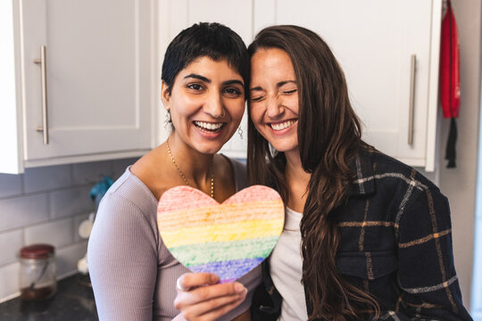Authentic shot of happy lesbian couple holding a heart shaped rainbow flag