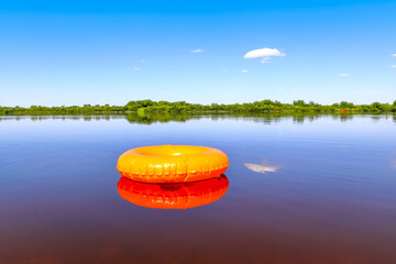 An orange inflatable swim ring is reflected in the river water. Summer rest