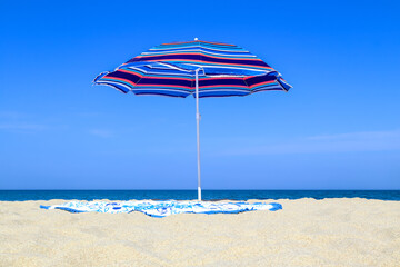 Beach umbrella, round towel on the sand. Shore sea