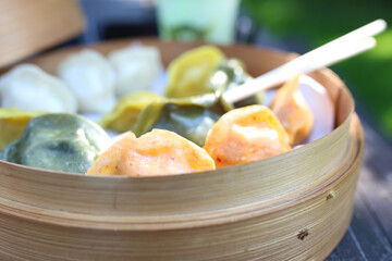 Traditional Chinese dumplings in a bamboo steamer basket. Colorful dim sum cooked on steam, close-up, selective focus.