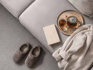 Cashmere sweater, reading and serving tray on gray sofa. Warm weekend at home aesthetics. Detail of...