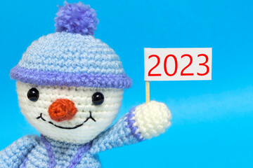snowman with a sign with the inscription 2023, on a blue background, new year concept