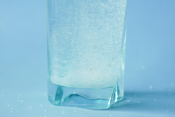 pouring white sugar in a glass of water on blue background 