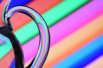 Ilusión óptica creada mediante la refracción de la luz con un recipiente de cristal lleno  de agua y líneas diagonales de colores	
