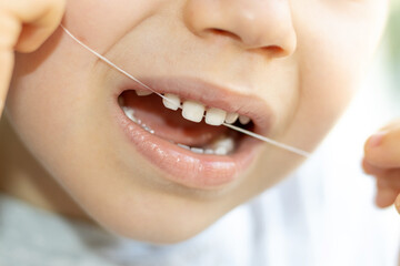 kid using dental floss to remove food rest from his milk teeth.child with spaces between teeth...